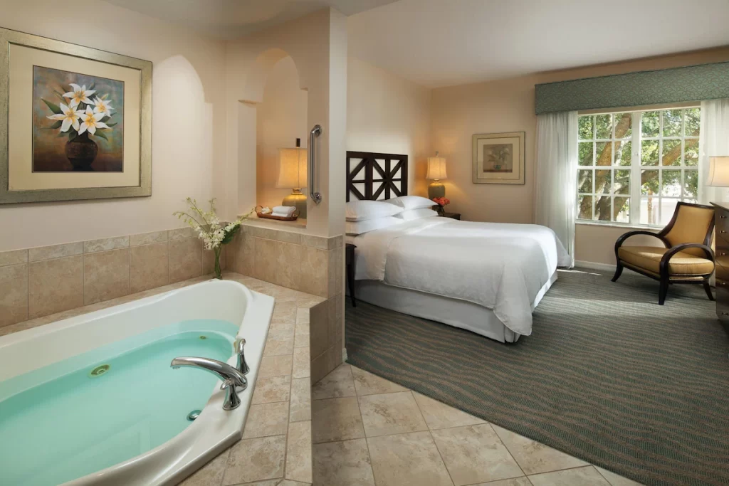 Hotel bedroom with a built-in jacuzzi tub near the bed, tiled floors, soft lighting, and classic decor